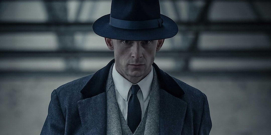 Homme en manteau sombre avec chapeau dans un cadre urbain.