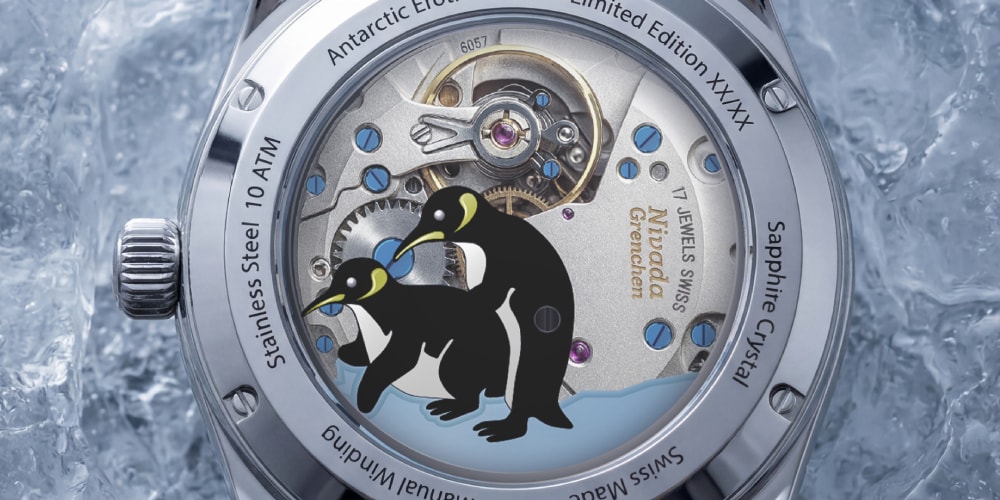 Montre avec fond transparent, deux manchots sur fond de mécanisme visible.