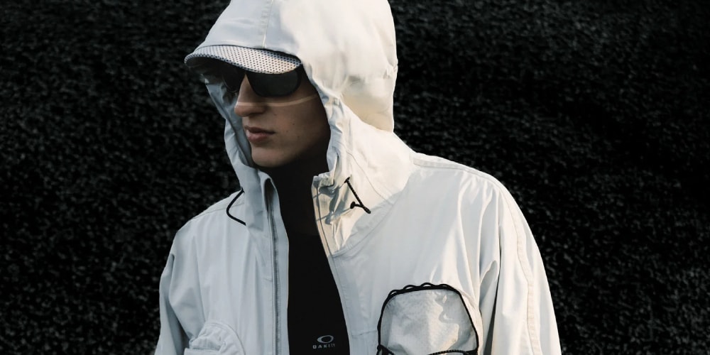 Personne en veste blanche avec capuche et lunettes noires, fond noir.