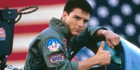 Pilote en combinaison devant un drapeau américain, pouce levé.