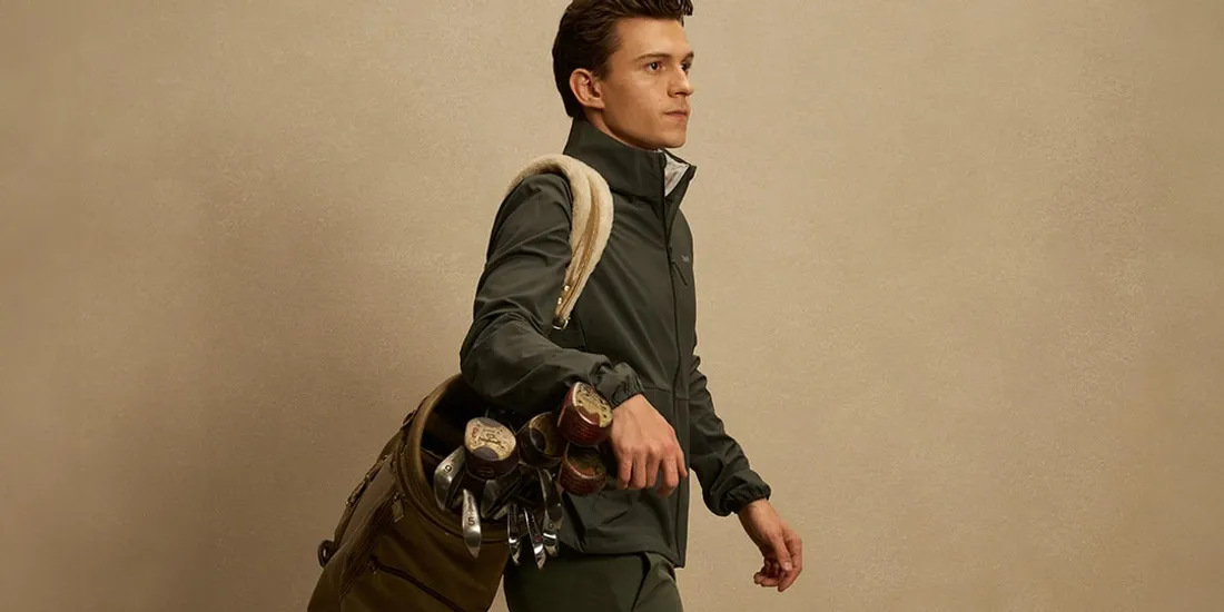 Homme avec sac de golf et clubs marchant sur fond beige.