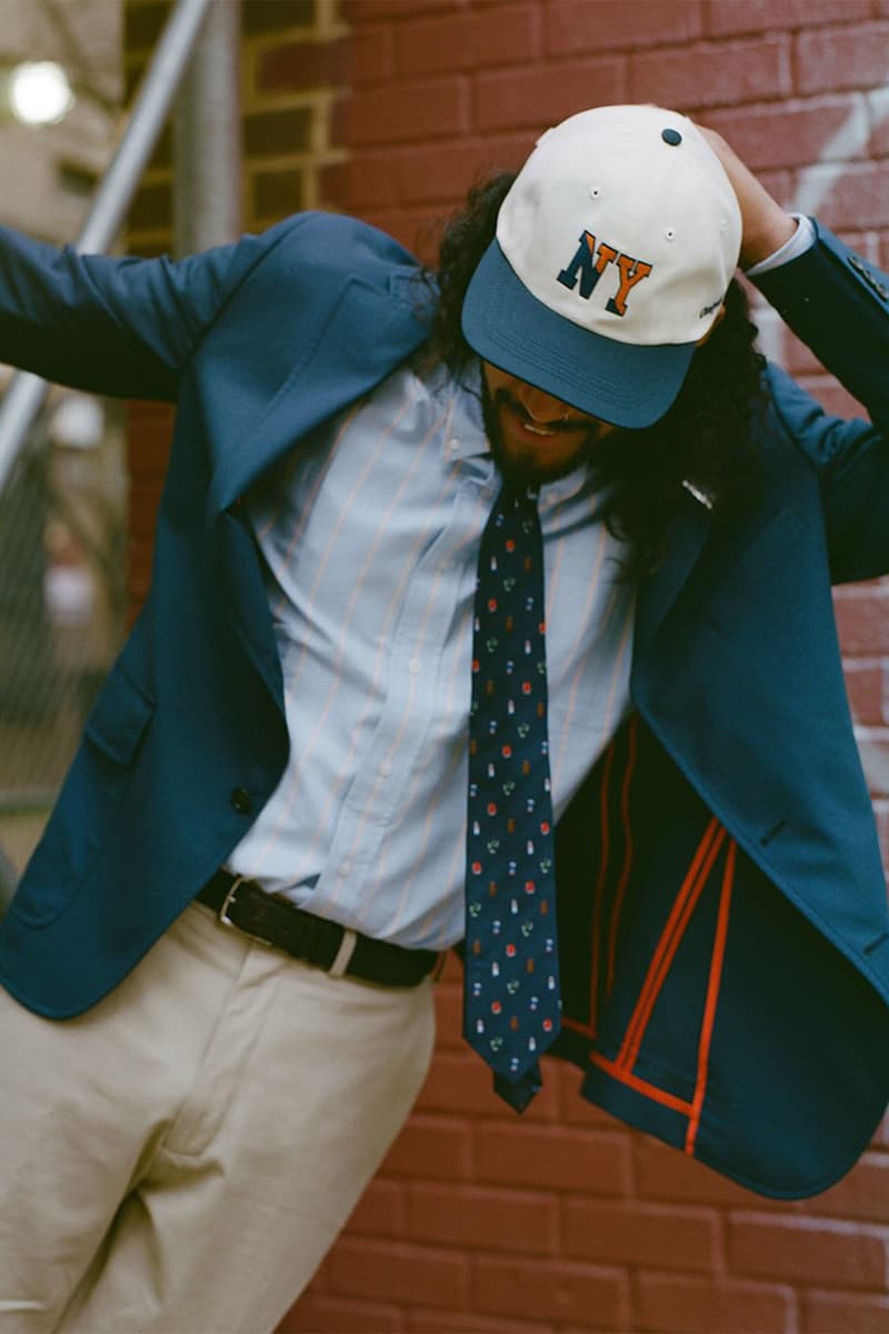 Homme en costume bleu, chemise rayée, cravate à motifs, casquette NY.