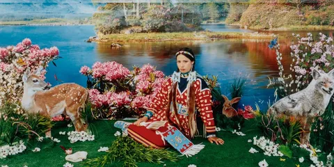 Personne en habit traditionnel devant un paysage floral et lacustre.