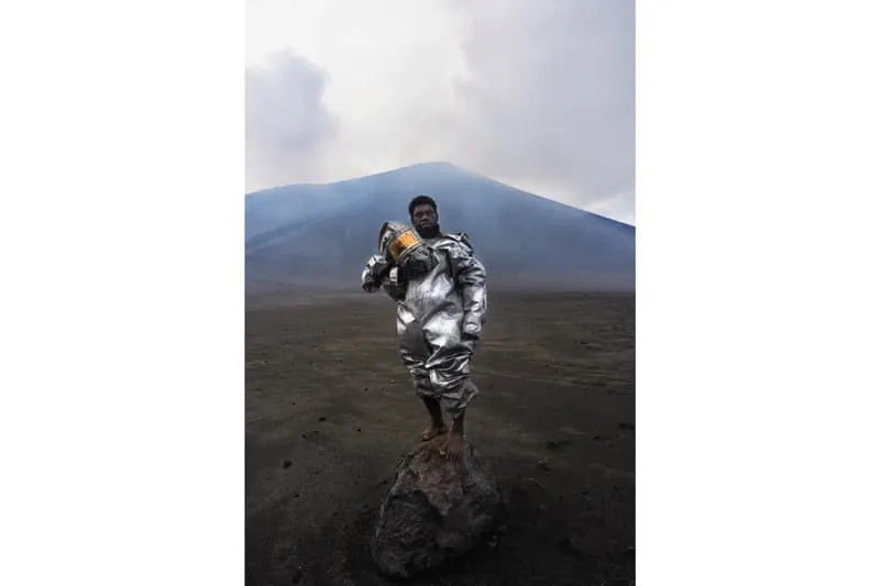 Personne en tenue argentée sur un rocher devant un volcan fumant