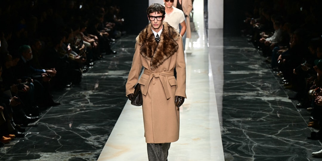 Défilé de mode homme avec manteau long et fourrure, sol marbré.