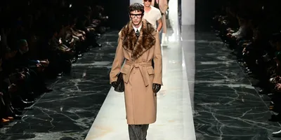 Défilé de mode homme avec manteau long et fourrure, sol marbré.