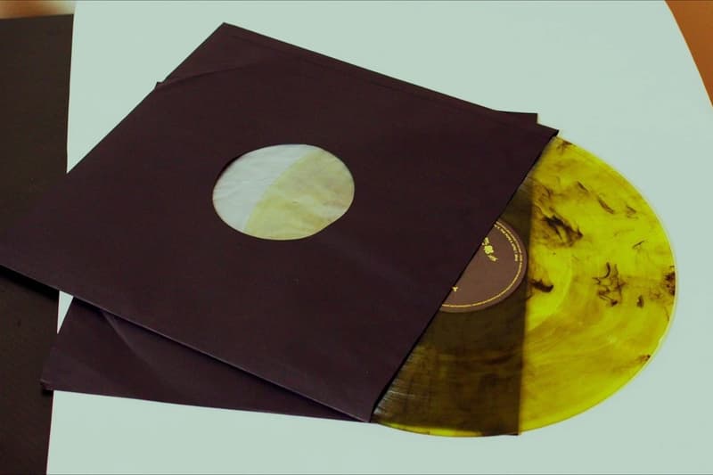 Disque vinyle jaune et noir dans une pochette noire sur une table.