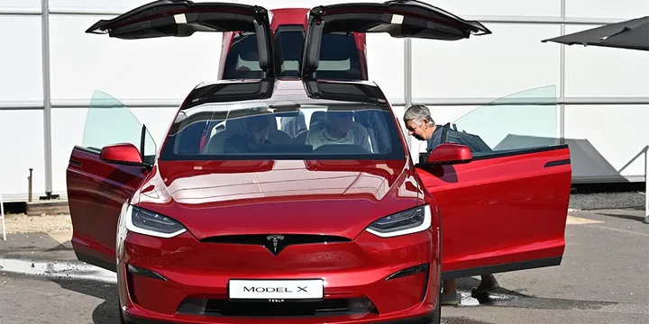 Voiture rouge Tesla Model X avec portes papillon ouvertes, personnes à l'intérieur.