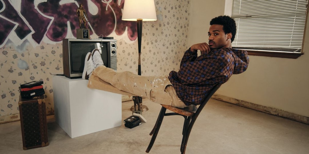 Homme assis sur une chaise, pieds sur une TV, graffiti en arrière-plan.