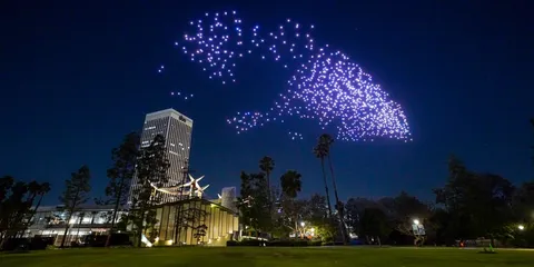Drones lumineux formant un motif dans le ciel nocturne au-dessus d'un parc.