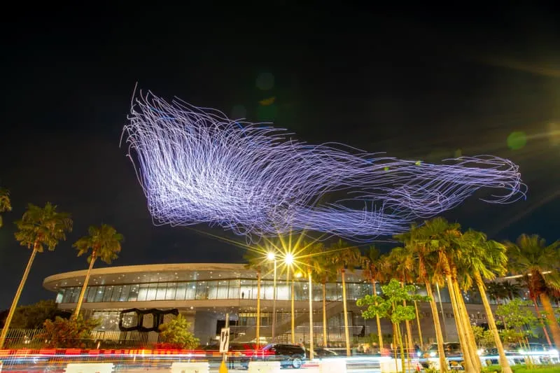Traînées lumineuses dans le ciel au-dessus d'un bâtiment moderne la nuit.