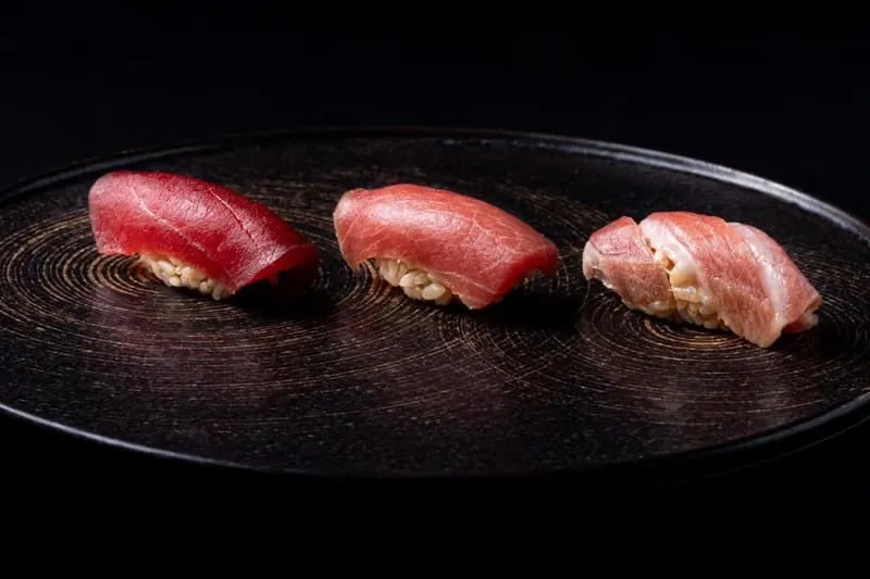 Trois sushis de thon sur une assiette noire.