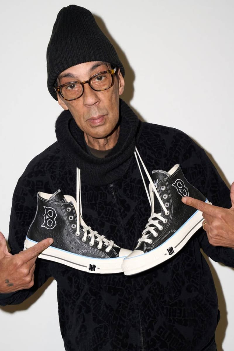 Homme avec des baskets noires, fond blanc, bonnet noir.