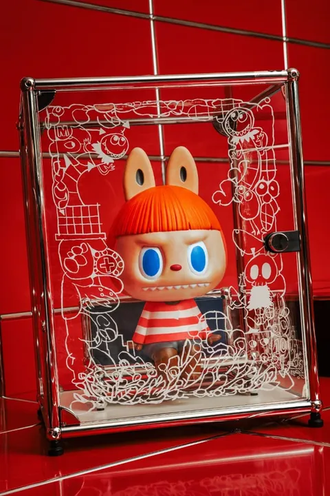 Figurine avec cheveux rouges et pulls rayés, boîte transparente décorée.