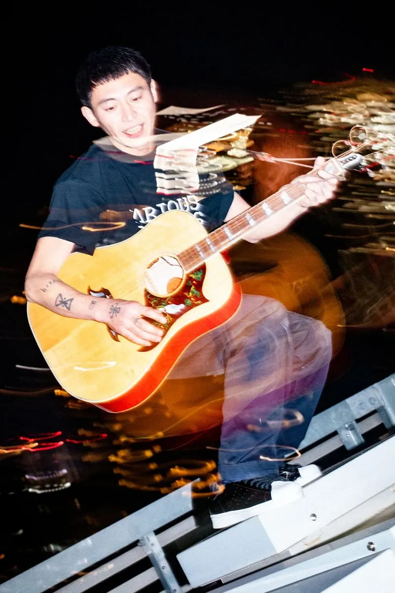 Homme jouant de la guitare avec un effet de mouvement flou, sur fond urbain nocturne.