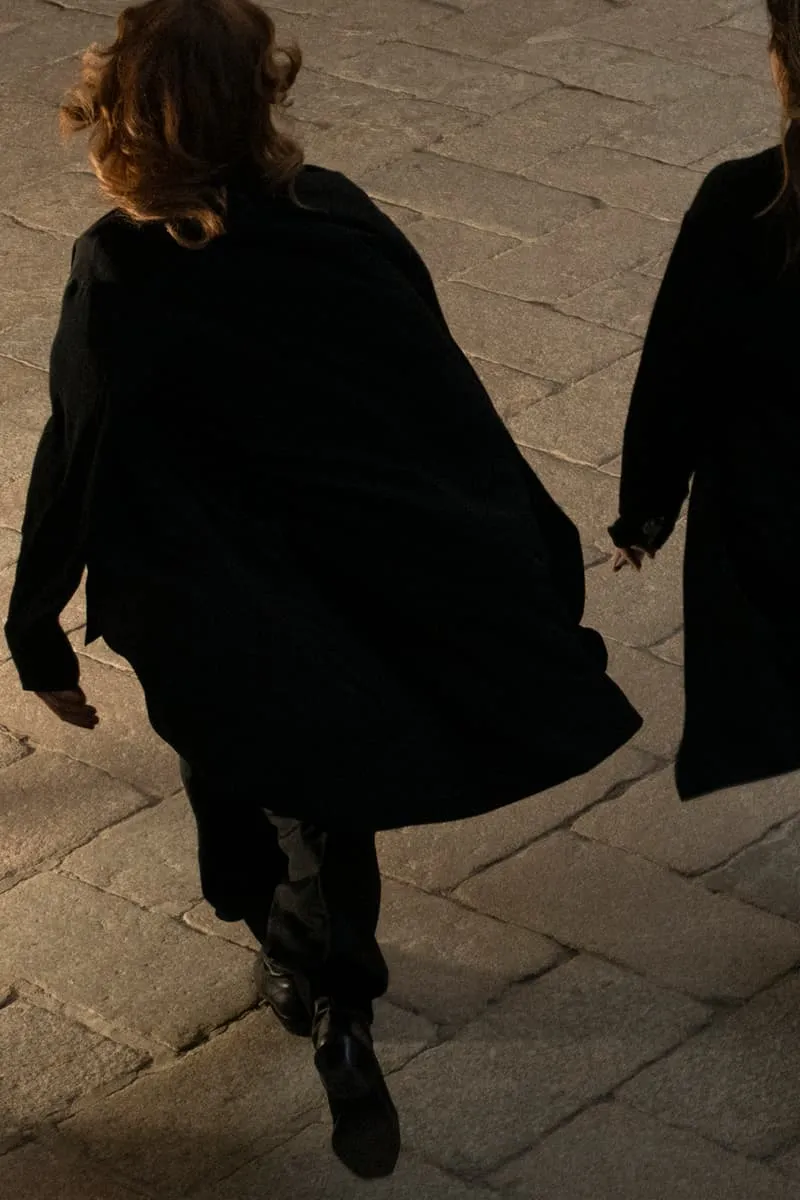 Deux personnes en manteaux noirs marchant sur des pavés.