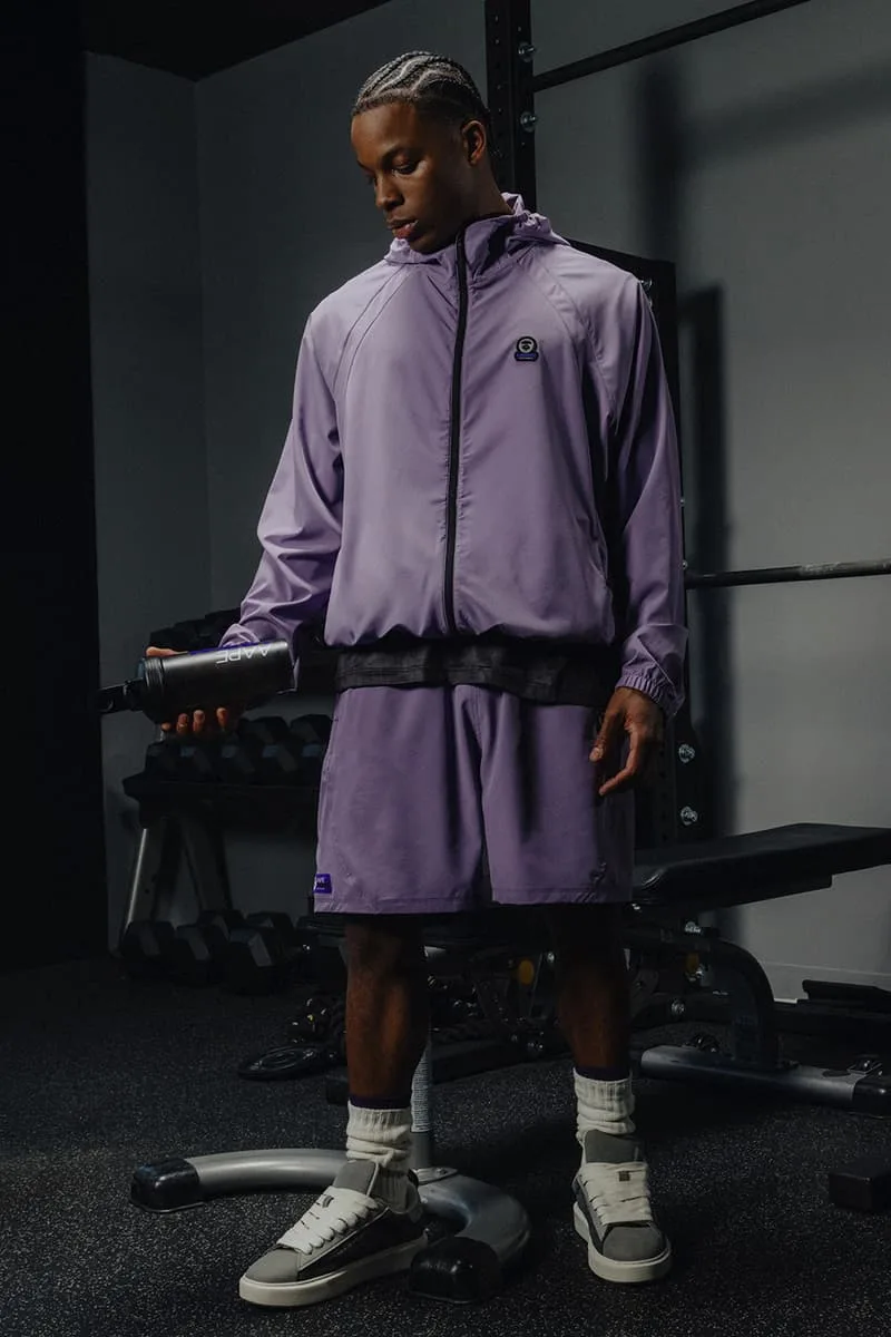 Homme en survêtement violet dans une salle de sport avec haltère.