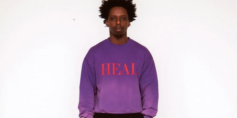 Homme en sweat violet avec 'HEAL' en rouge.