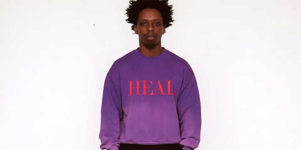 Homme en sweat violet avec 'HEAL' en rouge.