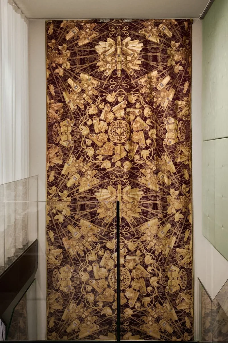 Grand tapis avec motifs dorés et complexes sur fond marron clair.
