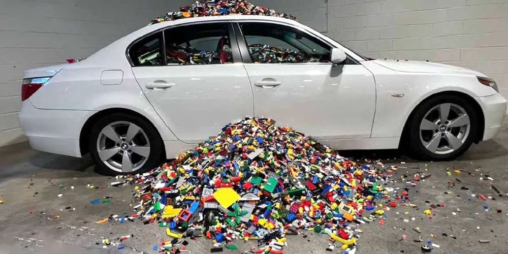 Voiture blanche submergée par des briques colorées amassées autour.
