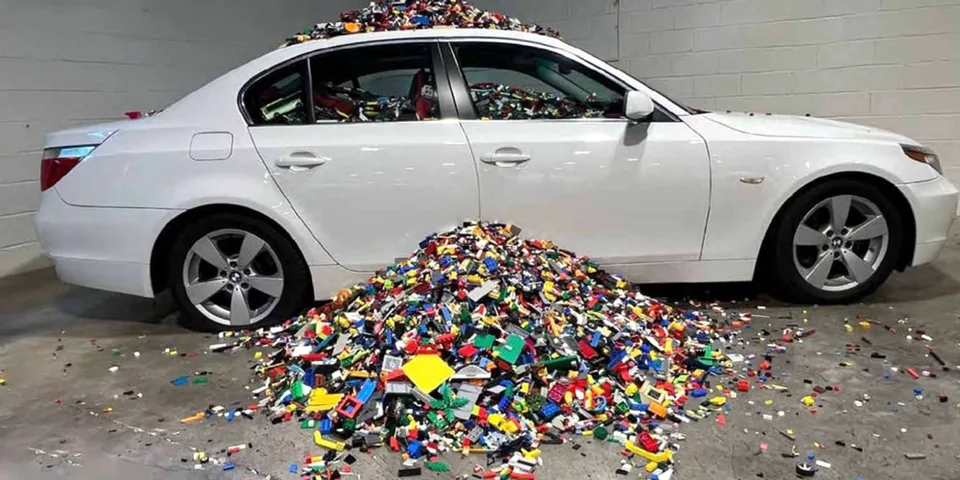 Voiture blanche submergée par des briques colorées amassées autour.