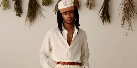 Homme en chemise blanche et casquette devant plantes séchées.