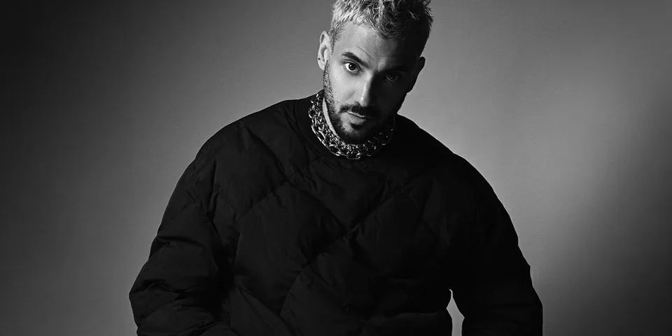 Homme avec des cheveux courts et barbe, portant un gros pull noir.