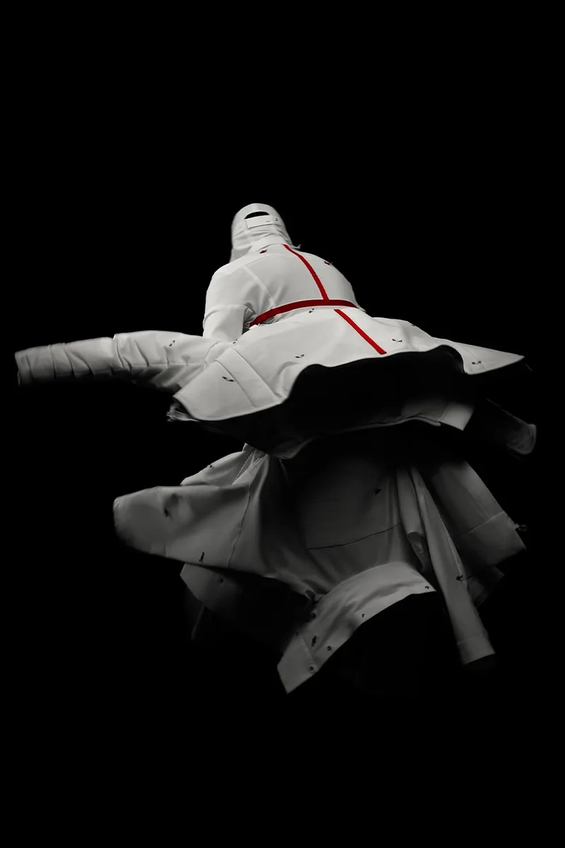 Danseur habillé en blanc sur fond noir réalisant une pirouette dynamique.