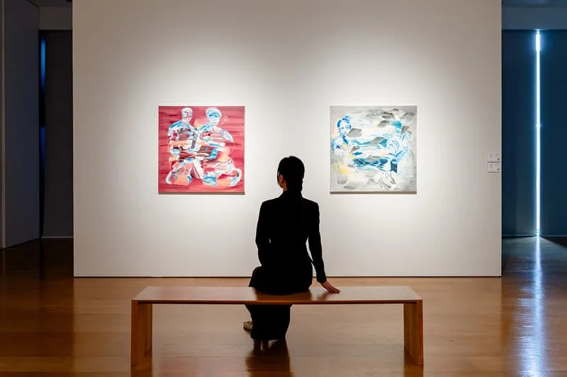 Personne assise devant deux peintures abstraites dans une galerie.