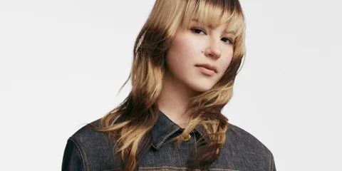 Personne avec une coiffure moderne portant une veste en jean, fond blanc.