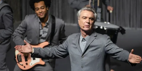 Homme en costume gris avec micro, en performance sur scène.