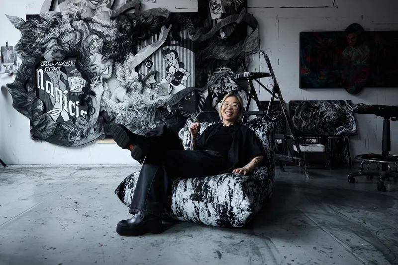 Femme souriante assise sur un fauteuil avec des œuvres d'art en arrière-plan.