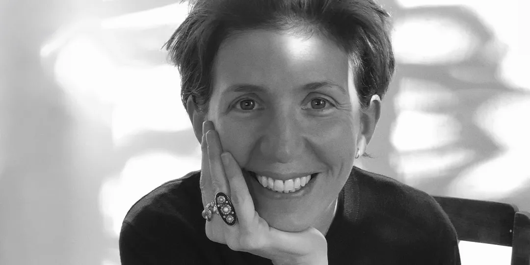 Femme souriante assise avec la main sur le visage, portant une bague.