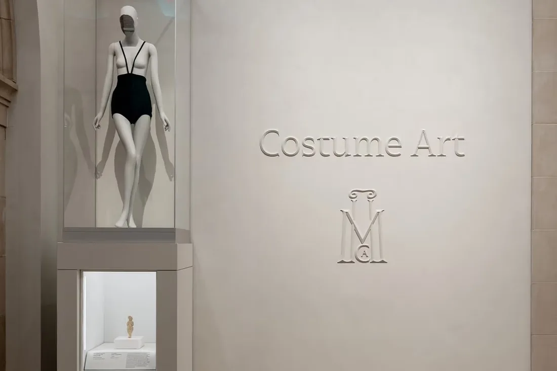 Statue en maillot de bain dans un musée avec 'Costume Art' sur le mur.