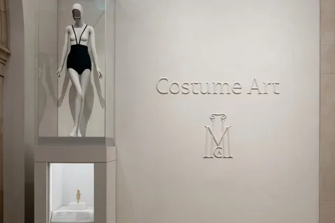 Statue en maillot de bain dans un musée avec 'Costume Art' sur le mur.
