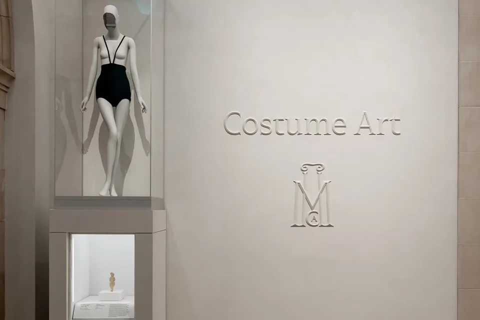 Statue en maillot de bain dans un musée avec 'Costume Art' sur le mur.