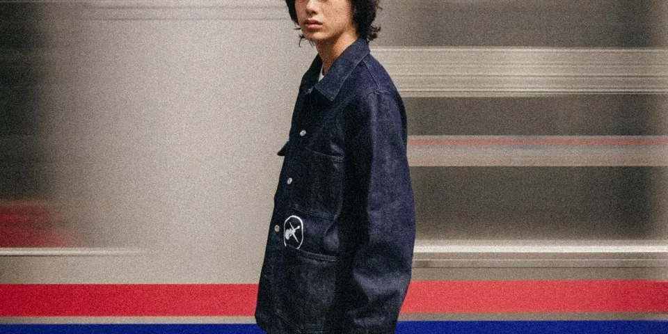 Personne en veste en jean devant un fond flou de train.