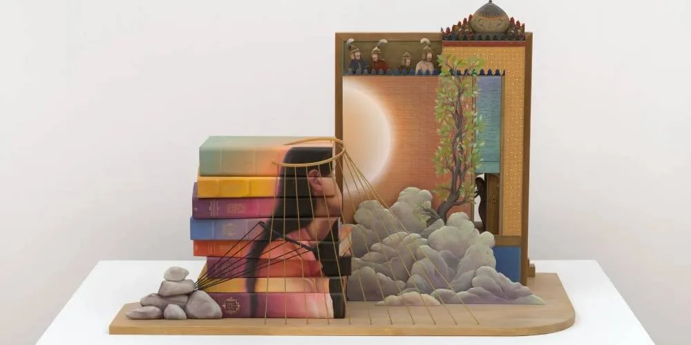 Sculpture livres et paysage avec personnage et fils tendus.