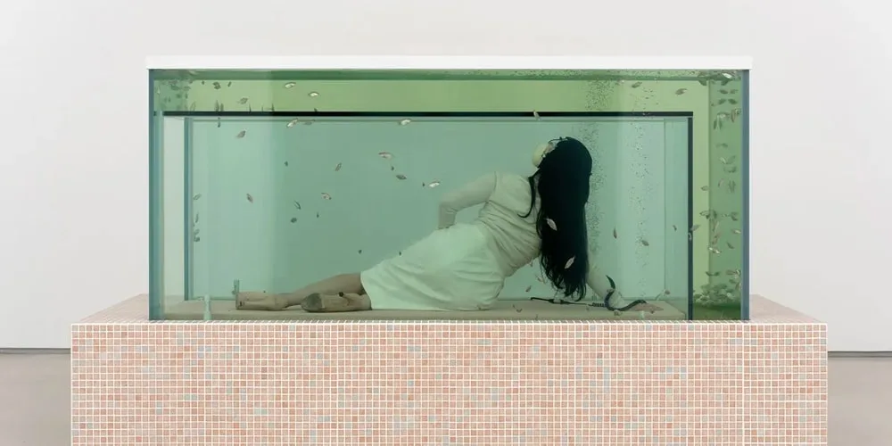 Femme allongée dans un grand aquarium avec des poissons nageant autour.