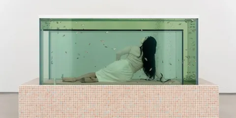 Femme allongée dans un grand aquarium avec des poissons nageant autour.