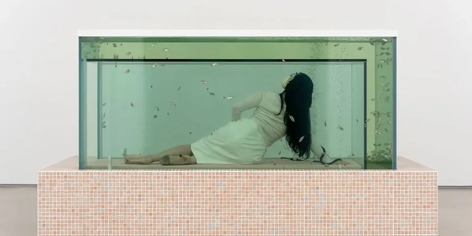 Femme allongée dans un grand aquarium avec des poissons nageant autour.