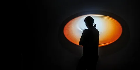 Silhouette d'une personne devant une lumière circulaire orange vif.