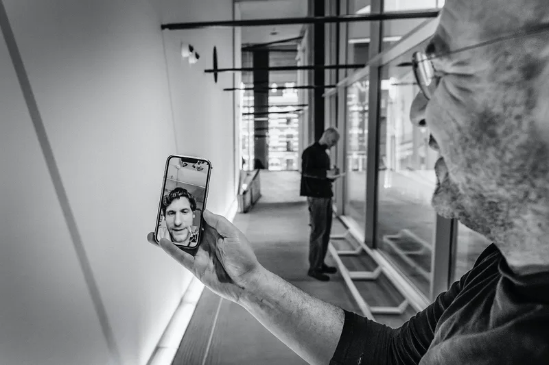 Un homme tient un téléphone montrant un appel vidéo avec un autre homme, en noir et blanc.