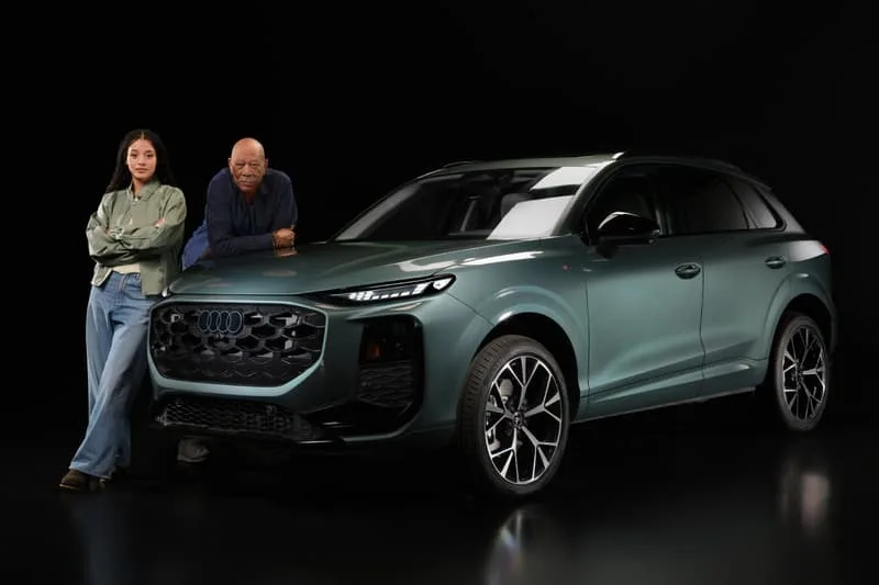 Deux personnes devant un SUV Audi vert foncé sur fond noir.