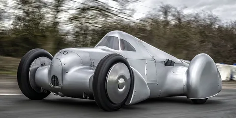 Voiture ancienne argentée sur une route, design rétro et aérodynamique.