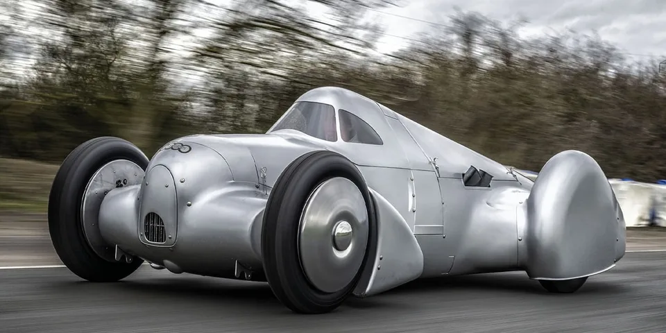 Voiture ancienne argentée sur une route, design rétro et aérodynamique.
