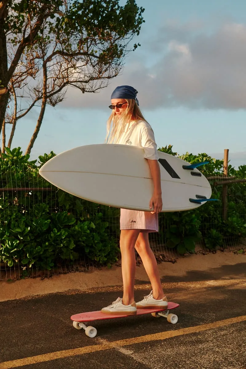 Personne skate avec une planche de surf sur un chemin ensoleillé.