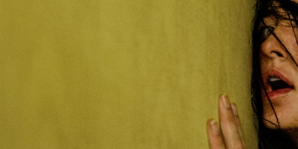 Visage partiellement visible d'une personne avec cheveux sombres contre un mur jaune.