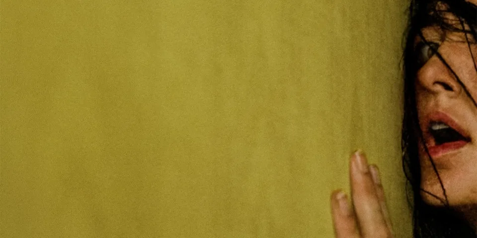 Visage partiellement visible d'une personne avec cheveux sombres contre un mur jaune.
